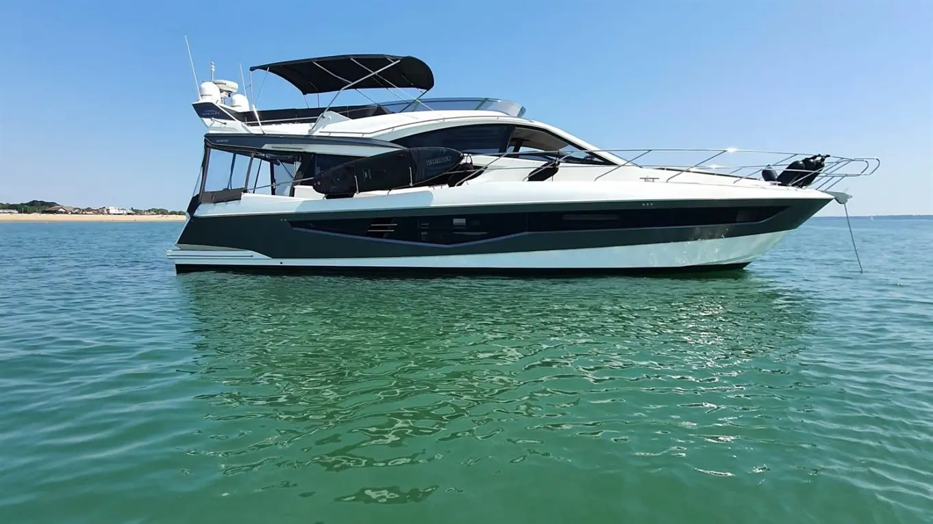 Luxury motor yacht anchored on clear blue water, with a sunny sky and shoreline visible in the background.